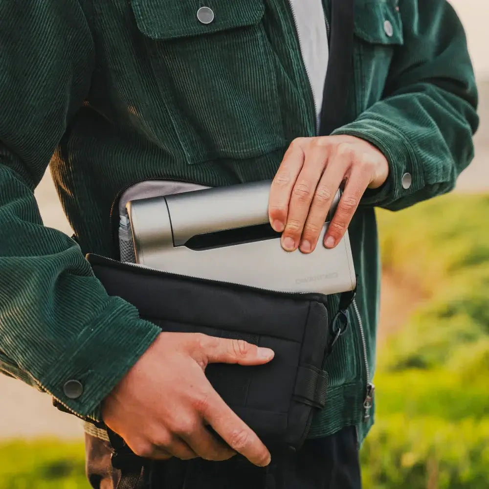 Person holding a black bag with a DWARF Telescope inside, outdoors.