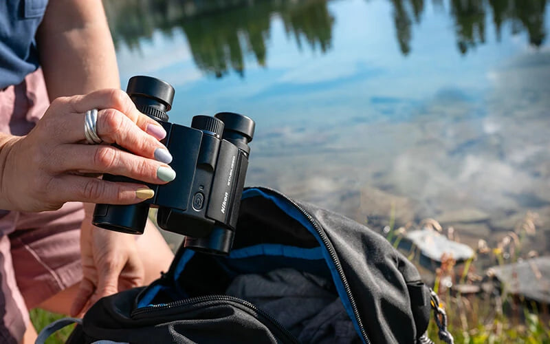 Person holding a pair of binoculars with a scenic background