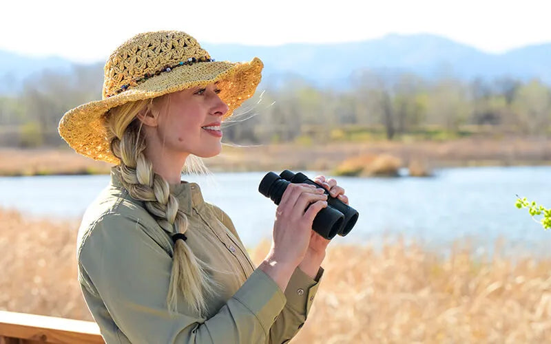Woman with binoculars by a lake with mountains in the background