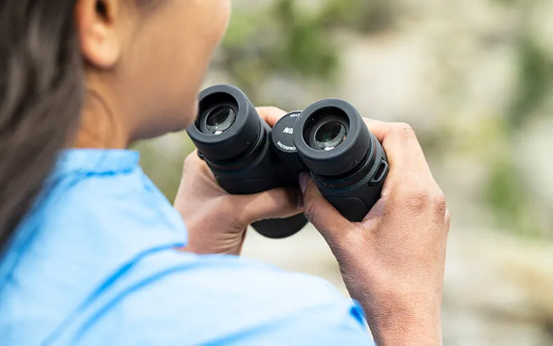Person holding binoculars with a blurred natural background