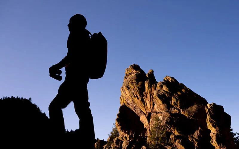 Silhouette of a hiker holding binoculars  with a backpack against a blue sky