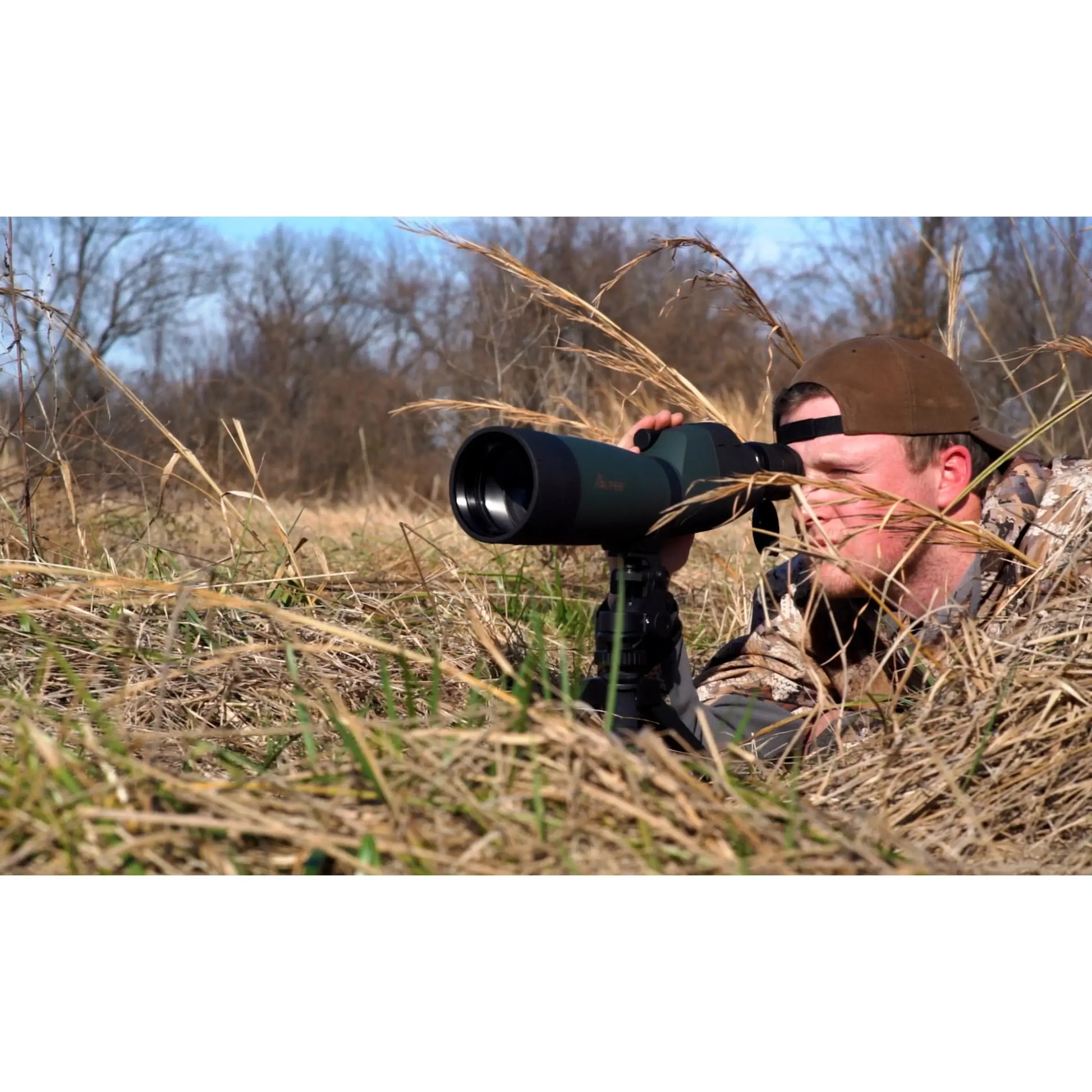 Birdwatcher laying beside some tall grass to use the Alpen Shasta Ridge 20-60x80 Waterproof Spotting Scope