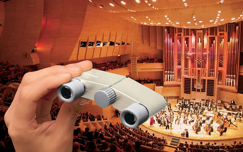 Hand holding binoculars over an orchestra in a concert hall