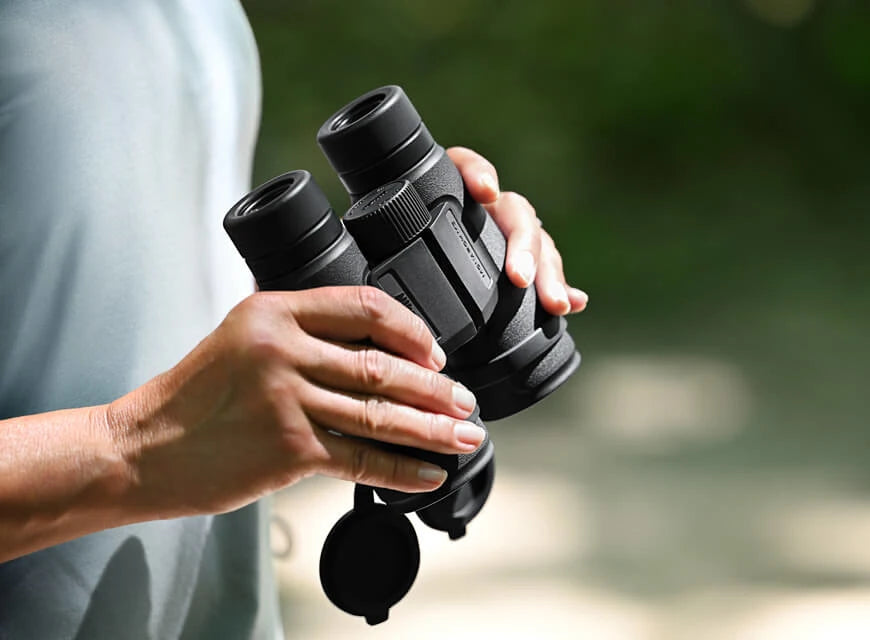 Nikon Monarch binoculars being held by a person with a blurred nature backgound.