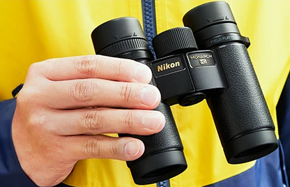 Person holding Nikon binoculars against a yellow background