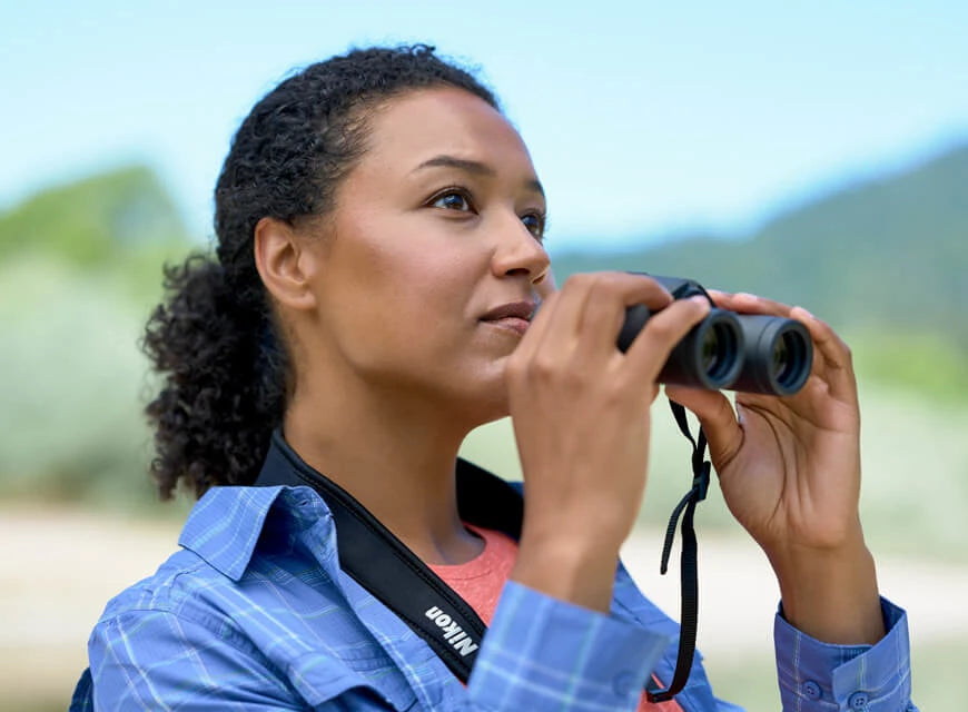 Person holding binoculars using them outdoors.