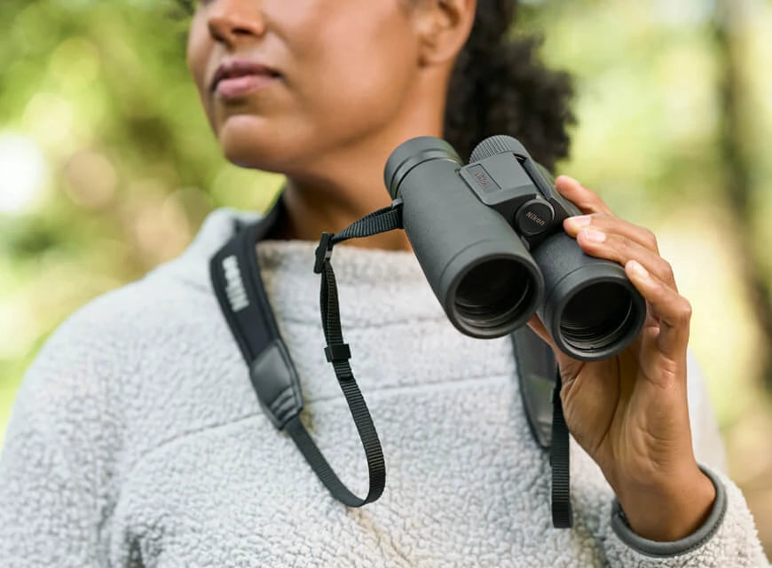Nikon Monarch M5 binoculars being held by a woman with a foliage filled, blurry background.