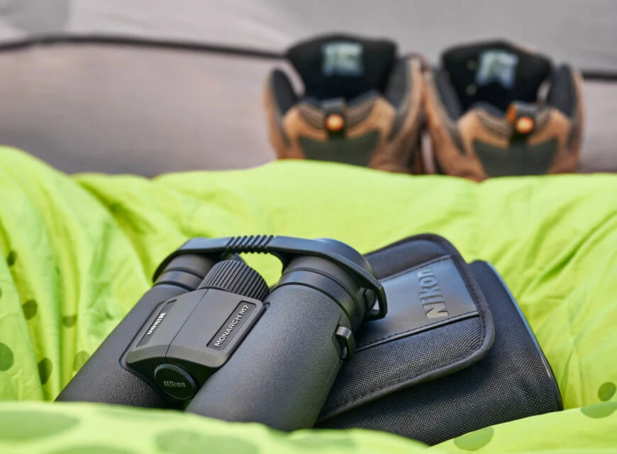 Binoculars sitting on some puffy fabric in a tent with footwear in the background.